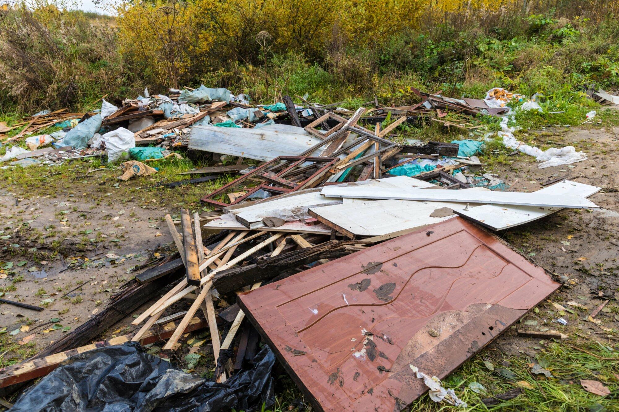 Stapel weggeworfener Holzbretter, Türen und verschiedener Abfälle lagen verstreut auf dem Boden in einer von Grün umgebenen Außenanlage und zeugten von den Folgen einer Garten-Entrümpelung.